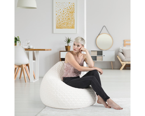 Eine Frau sitzt auf einem weißen Sitzsack in einem hellen Wohnzimmer.