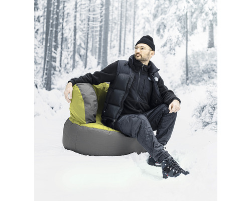 Mann sitzt in einem Sessel im Schnee vor einem verschwommenen Wald