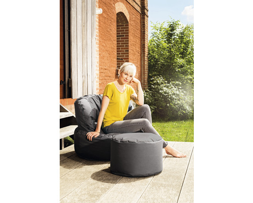 Eine Frau sitzt entspannt in einem grauen Sitzsackstuhl mit Fußhocker im Freien.