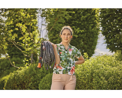 Frau hält einen Gartenschlauch im Garten