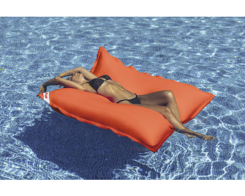 Frau liegt auf einer orangefarbenen Schwimminsel im Pool.