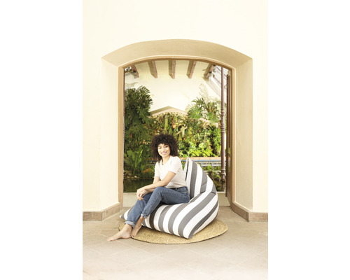 Frau sitzt auf einem gestreiften Sitzsack auf einem geflochtenen Teppich