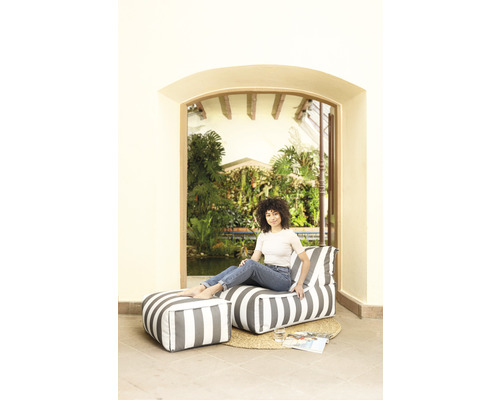Frau sitzt in einem Zimmer auf einem gestreiften Sitzsack mit Fußhocker