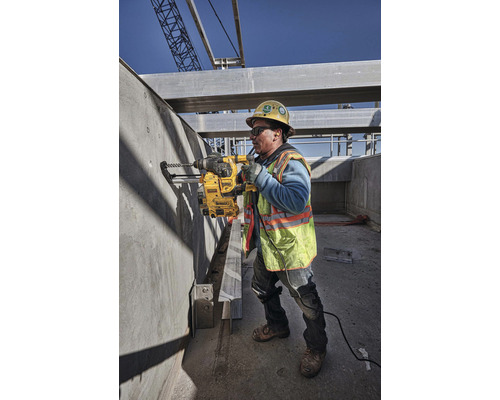 Ein Bauarbeiter bohrt mit einer Bohrmaschine ein Loch in eine Betonwand auf einer Baustelle.