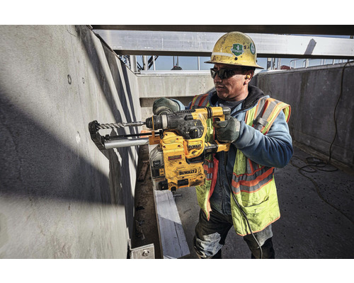 Ein Bauarbeiter bohrt mit einer DeWalt Bohrmaschine in eine Betonwand auf einer Baustelle.