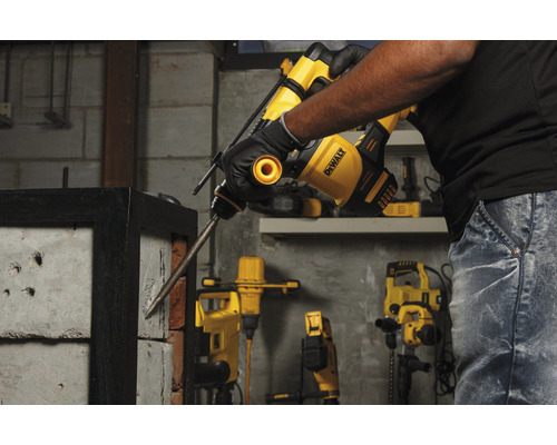 Ein Mann benutzt einen Bohrhammer von DeWalt, um in eine Ziegelwand zu bohren.