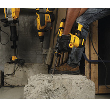 Ein Handwerker benutzt einen Abbruchhammer von DeWalt, um Beton zu bearbeiten. Weitere Bohrhämmer stehen im Hintergrund bereit.