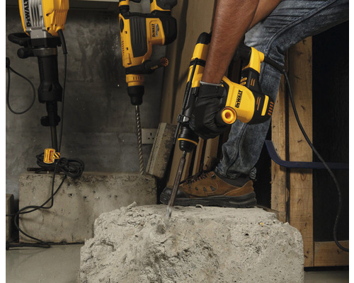 Ein Handwerker benutzt einen Abbruchhammer von DeWalt, um Beton zu bearbeiten. Weitere Bohrhämmer stehen im Hintergrund bereit.