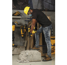 Ein Arbeiter mit Schutzhelm benutzt einen Bohrhammer, um ein Stück Beton zu bearbeiten.