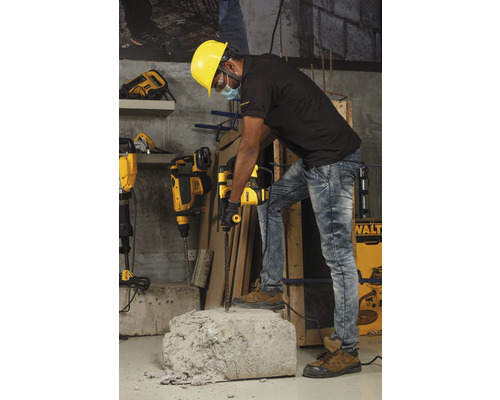 Ein Arbeiter mit Schutzhelm benutzt einen Bohrhammer, um ein Stück Beton zu bearbeiten.