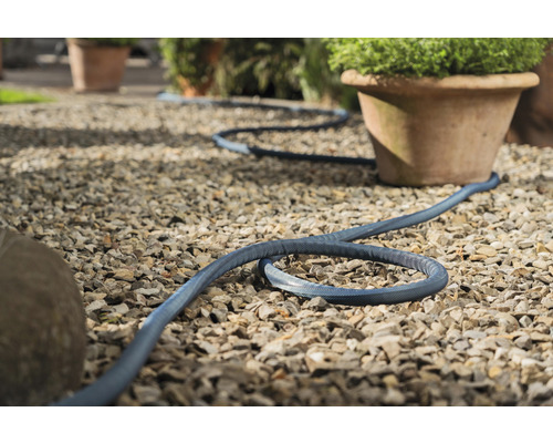 Blauer Gartenschlauch liegt auf Kiesweg neben Pflanzentöpfen.