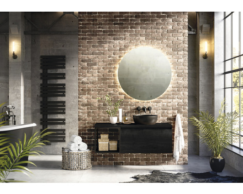 Modernes Badezimmer mit Waschtisch, rundem Spiegel, Handtuchwärmer und Badewanne vor einer Backsteinwand