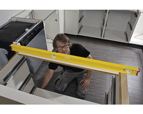 Handwerker überprüft mit einer Wasserwaage die Ausrichtung einer Küchenzeile bei der Montage.