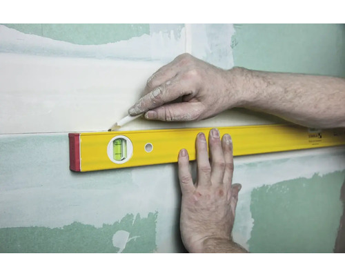 Eine Wasserwaage wird an einer Wand mit Gipsplatten angelegt, um eine Linie mit einem Bleistift zu zeichnen.