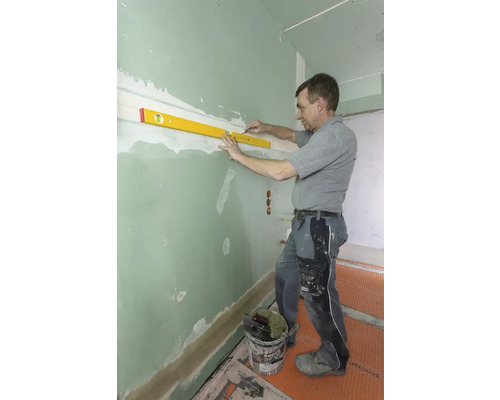 Handwerker richt Wand mit Wasserwaage aus.