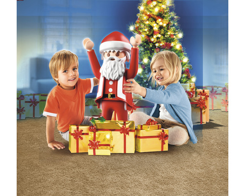 Zwei Kinder mit einer Playmobil-Weihnachtsfigur und Geschenken vor einem Weihnachtsbaum.