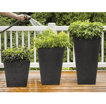 Drei bepflanzte, quadratische Pflanzgefäße unterschiedlicher Größe werden mit einem Gartenschlauch bewässert.
