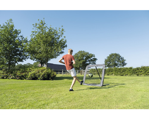 Junge schießt Fußball in ein tragbares Fußballtor im Garten.