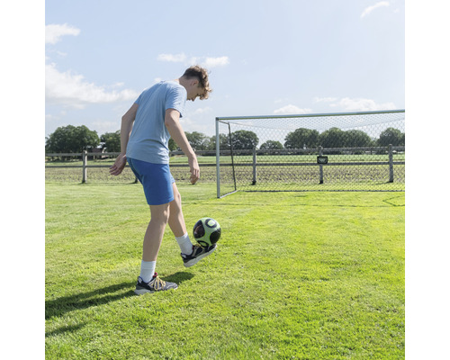 Junge spielt mit Fußball vor Fußballtor im Garten