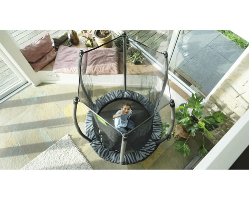 Kind auf einem runden Gartentrampolin mit Sicherheitsnetz in einem Wintergarten