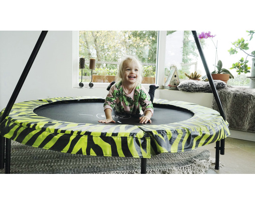 Ein Kind liegt lachend auf einem runden Trampolin mit Tiermuster im Innenbereich.