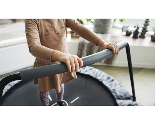 Kind springt auf einem runden, grauen Trampolin mit Haltegriff.