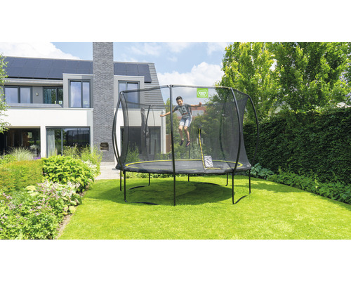 Junge springt auf einem Gartentrampolin mit Sicherheitsnetz vor einem modernen Haus