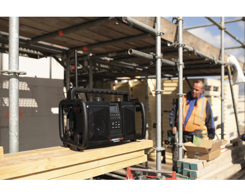 Baustellenradio auf einer Holzoberfläche mit einem Bauarbeiter im Hintergrund