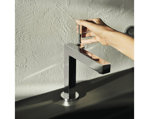 Hand betätigt einen verchromten, eckigen Wasserhahn im Badezimmer