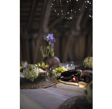 Dekorativer Tisch mit Artischocken, Gläsern, Blumenvase und Lichterketten unter kugelförmigen Lampen.