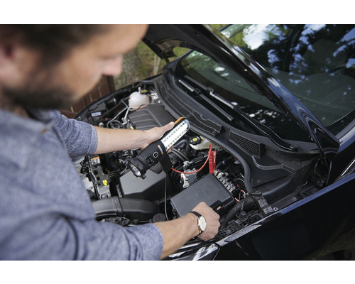 Eine Person verwendet eine LED-Arbeitsleuchte zur Inspektion des Motorraums eines Autos.