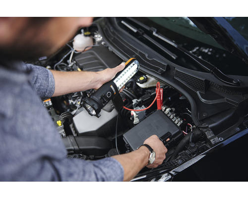 Eine Person beleuchtet mit einer LED-Arbeitsleuchte einen Motorraum.