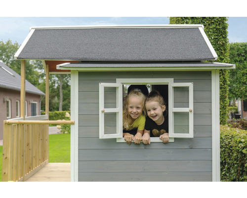 Zwei Kinder schauen aus dem Fenster eines grauen Holzspielhauses mit grauem Dach