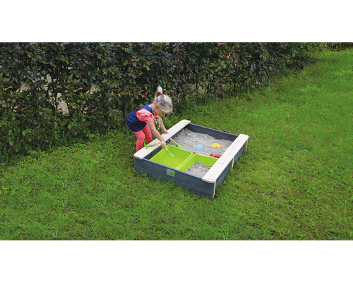 Kind spielt in einem Sandkasten mit Holzeinfassung und Sandspielzeug im Garten.