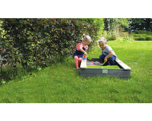 Kinder spielen in einem Sandkasten mit grünen Behältern im Garten.