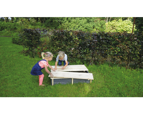 Zwei Kinder spielen an einem Sandkasten mit Deckel im Garten.
