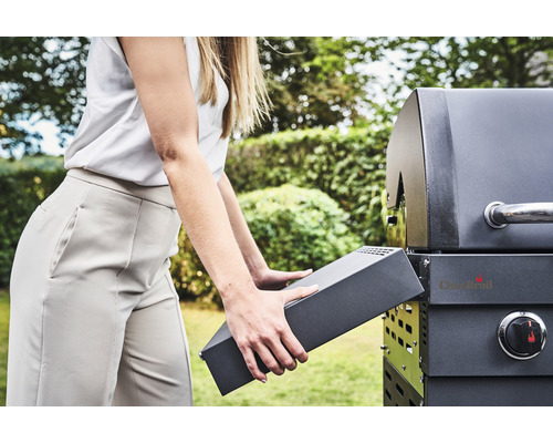 Eine Person setzt ein Seitenteil an einem Holzkohlegrill an.