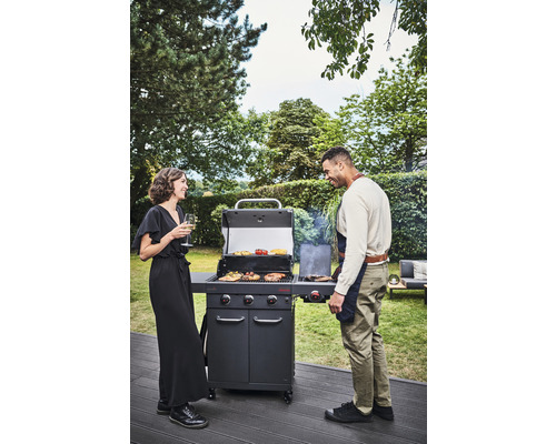 Szene mit einem Grill, zwei Personen und Grillgut im Garten.