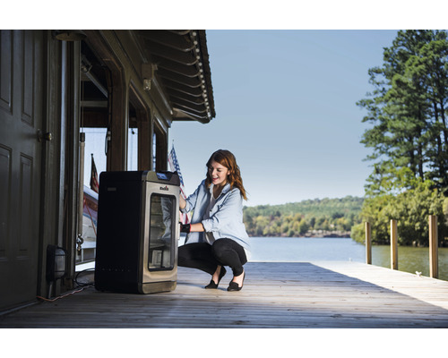 Frau benutzt Räucherofen im Freien in der Nähe von Gewässer