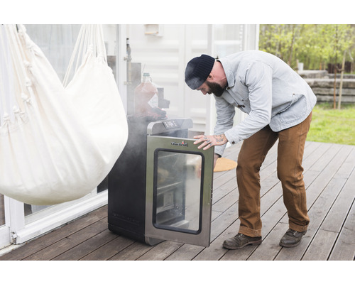 Mann öffnet elektrischen Räucherofen der Marke Char-Broil auf einer Terrasse.