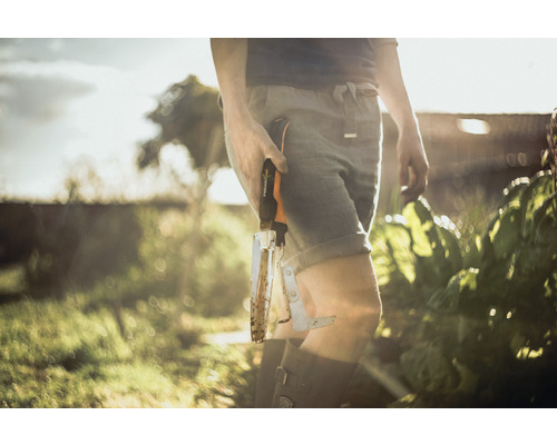 Eine Person hält eine gebrauchte Fiskars Unkrautstecher im Garten