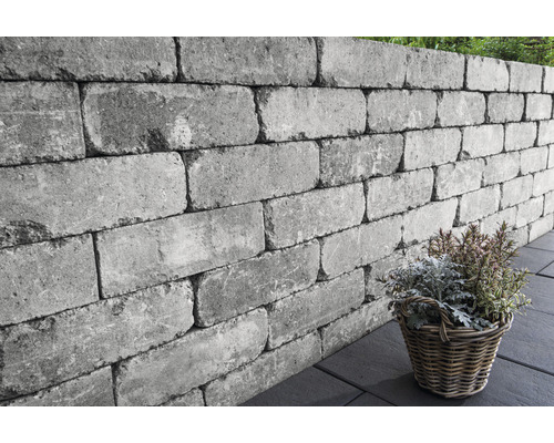 Graue Mauersteine bilden eine Gartenmauer mit Korb
