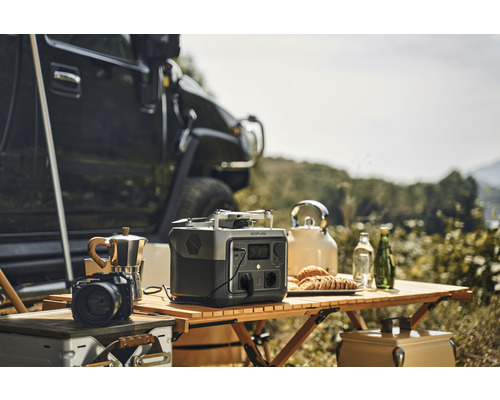 Szene mit einem tragbaren Ecoflow-Kraftwerk, einer Kaffeemaschine, einer Kamera, einer Drohne und einem Teekessel auf einem Holztisch im Freien