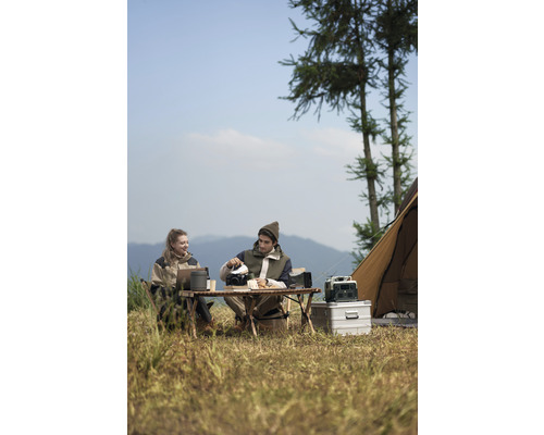 Zwei Personen beim Camping mit Tisch, Stühlen, Kochutensilien und Zelt in der Natur