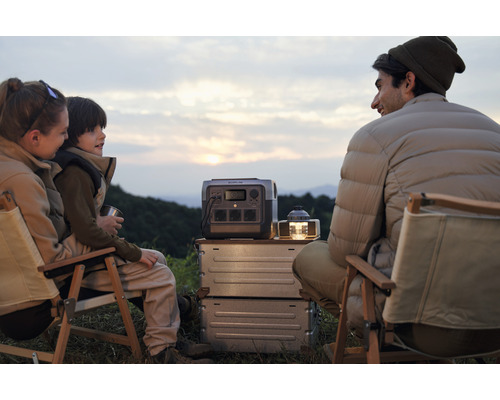 Familie sitzt beim Camping mit tragbarer Powerstation und Lampe