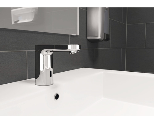 Berührungsloser Waschtischmischer auf einem weißen Waschbecken mit dunklen Fliesen im Hintergrund