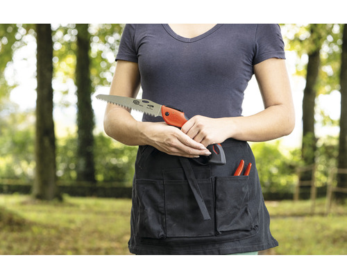 Eine Frau hält eine Handsäge vor einer Gartenschürze