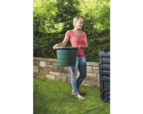 Frau trägt grünen Eimer im Garten zum Kompost.