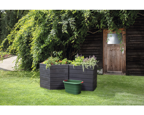 Zwei dunkle Hochbeete mit Bepflanzung und eine grüne Gartentonne im Garten.