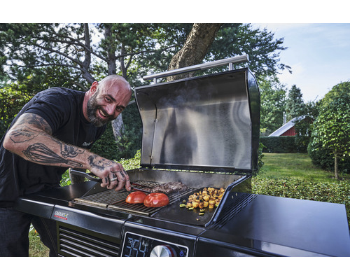 Mann grillt Gemüse und Fleisch auf einem Holzkohlegrill im Garten.
